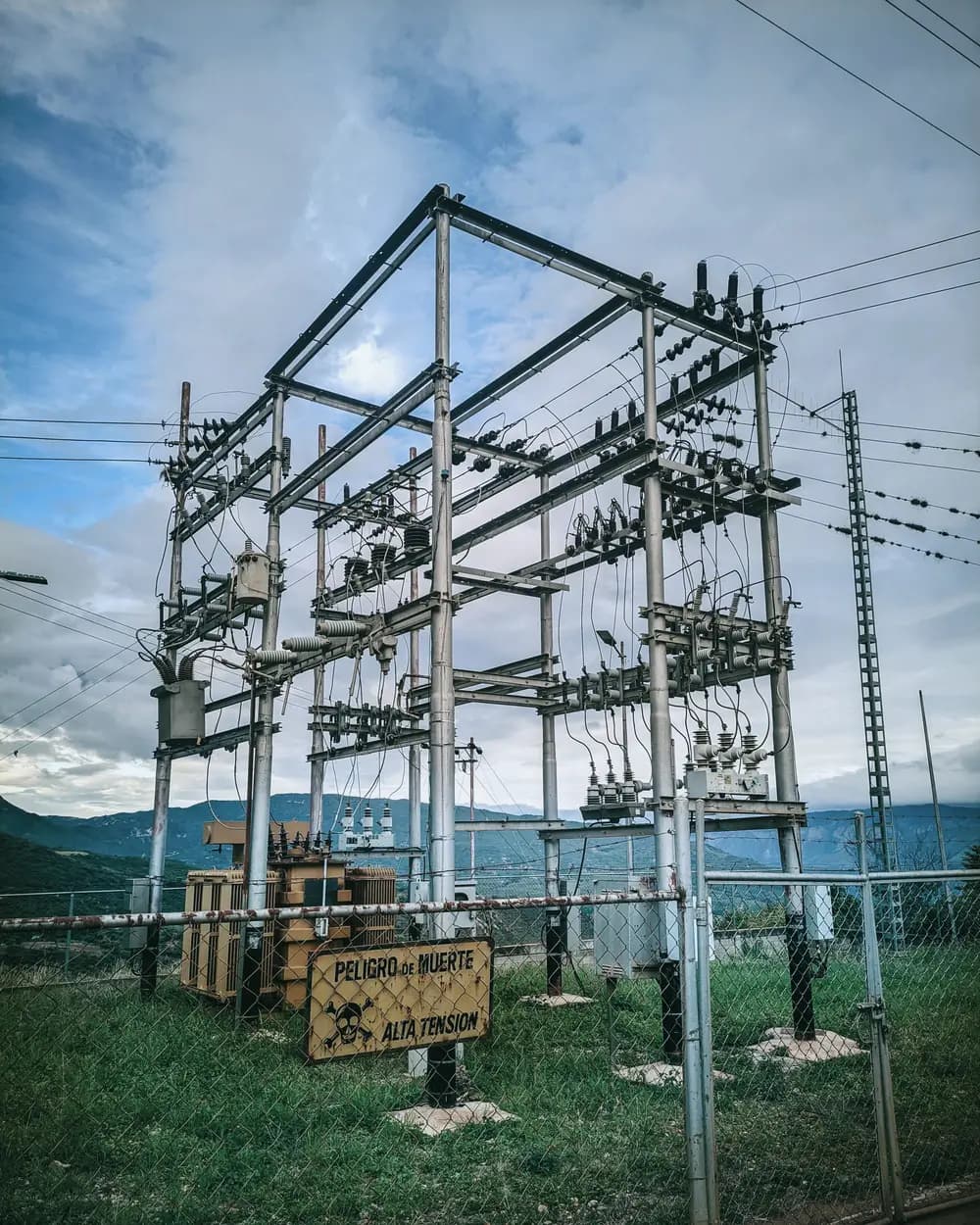 Subestación eléctrica rural con un letrero de advertencia, en un día nublado