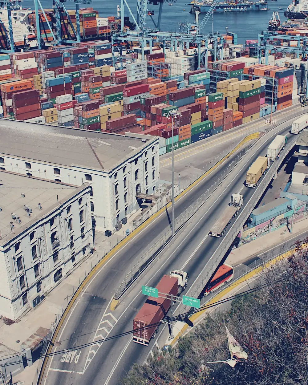 Camiones bajando hacia el puerto de Valparaíso, con la cancha de contenedores al fondo