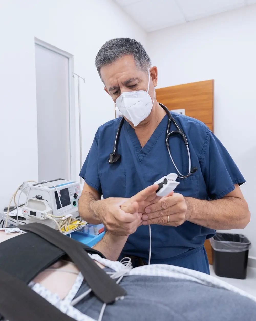 Médico con mascarilla y uniforme clínico conectando un oxímetro al dedo de un paciente acostado